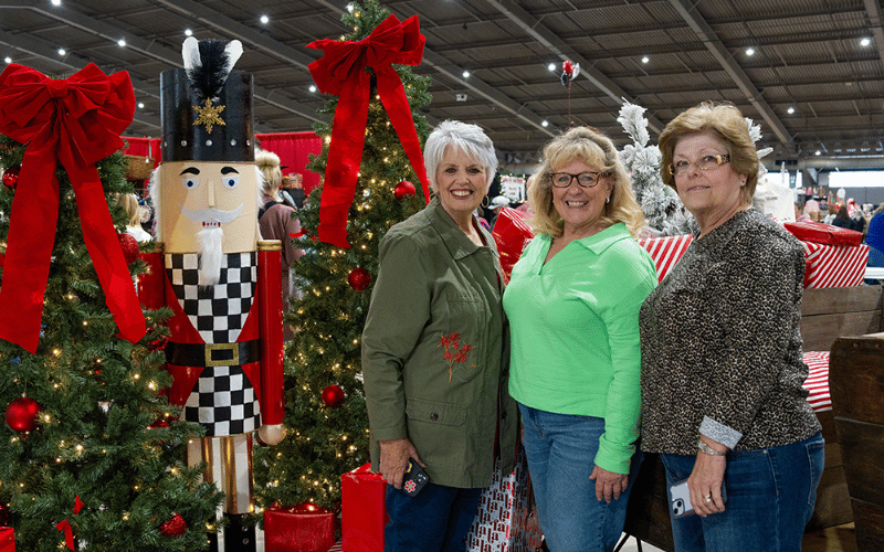 3 smiling white Women Posing for photo next to giant nutcracker at affair of the heart show