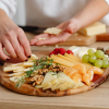 A person layering slices of cheese on a charcuterie board