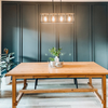 Brown kitchen wooden table with floral centerpiece, four hanging lights and a green painted wall