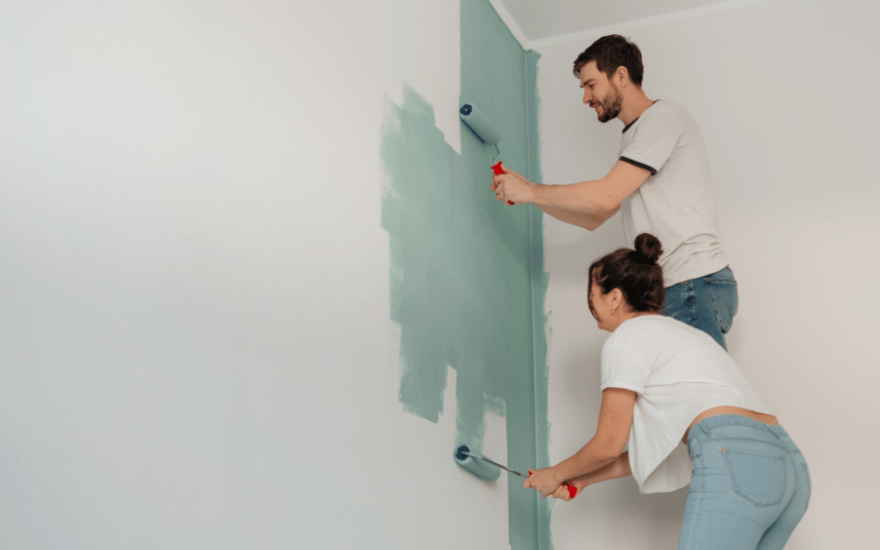 young caucasian couple wearing white tshirts and blue jeans painting a wall teal using rollers