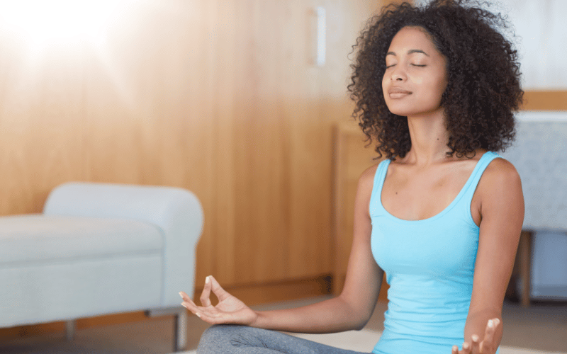 African american woman wearing light blue tank top doing yoga and meditating on the floor