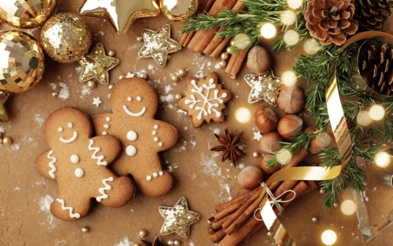 Home Made Iced Gingerbread Men on brown table top next to flour, Christmas decorations and cinnamon sticks