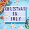 Christmas in July on film board on baby blue background surrounded by flip flops, starfish and evergreen garland