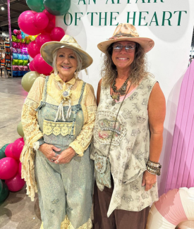 Two blonde women in their 40s or 50s dressed western posing smiling at the camera in front of the AOTH sign