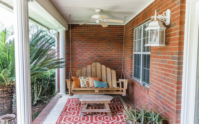 Front porch with red and white rug underneath picnic table and wooden swing