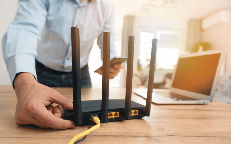 hands adjusting wifi router next to laptop