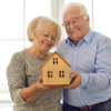 Senior Citizen Couple holding wooden miniature of a house