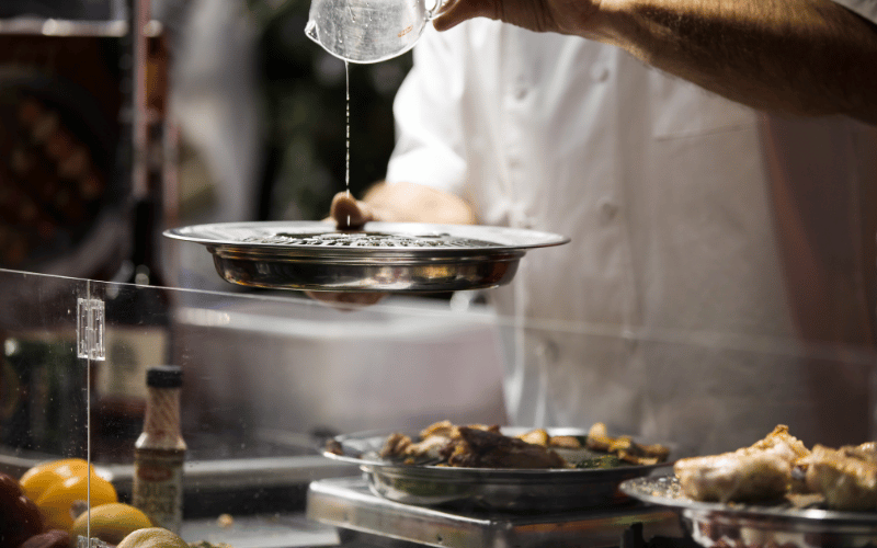 Chef-in-kitchen-pouring-oil-into-dish-cooking