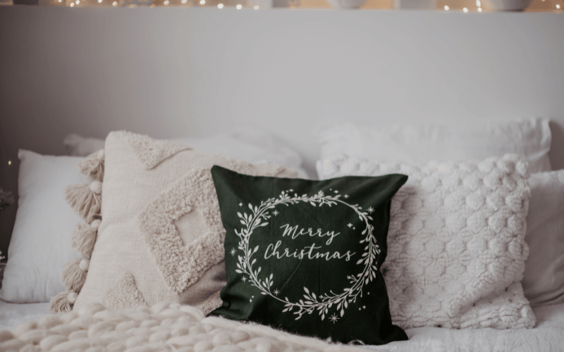 White couch throw pillows along with a green decorative pillow that says Merry Christmas on it