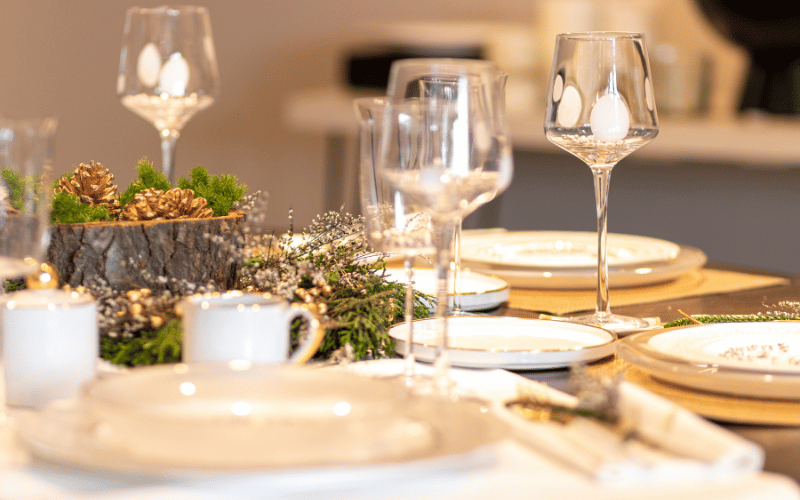 Close up of classy gold themed Christmas table setting with pinecone and pine centerpiece and wine glasses