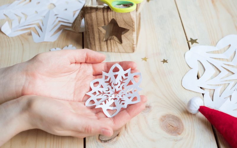 Small hands holding home made paper snowflake DIY decoration against wooden table