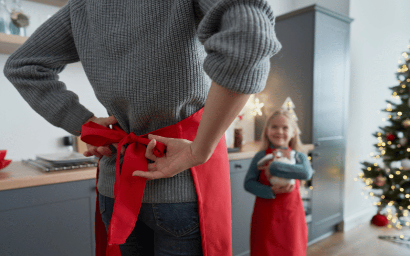 Close up of white female tying up a red apron about to bake cookies with her young blonde daughter