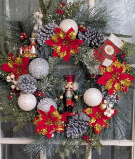 Holiday Wreath with red poinsettas and silver and white bulbs with a nutcracker in the middle