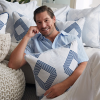 Mini version of Craig Conover posing smiling clutching blue and white pillows in front of white couch sitting on floor