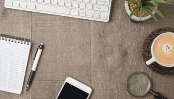 Close up of flat lay over desk with keyboard, coffee, note pad, pen, houseplant and iphone
