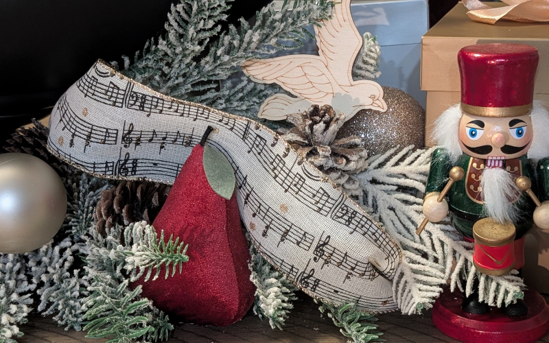 Katherine Brooke Design amusic themed ribbon, next to fake Christmas greenery, an ivory bulb and a nutcracker