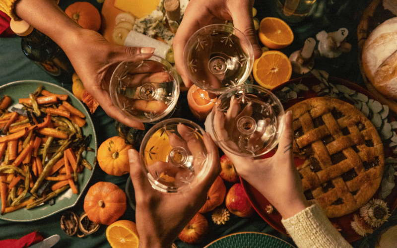 four friends cheersing white wine glasses over Thanksgiving dinner spread