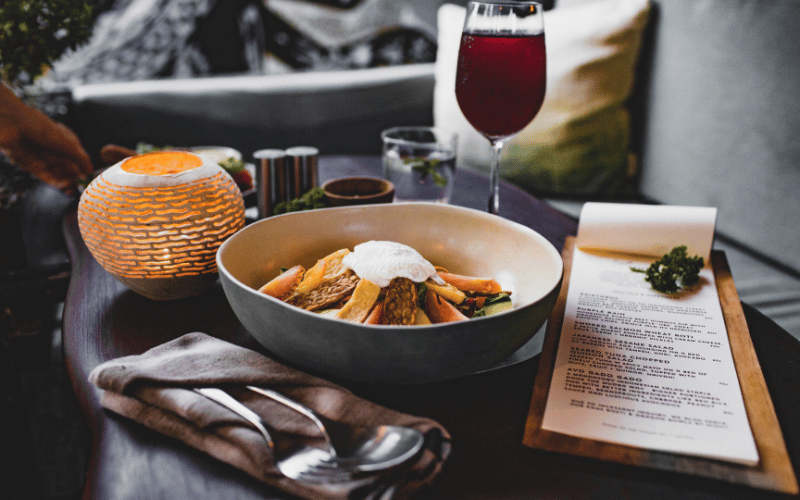 Fall grains dinner bowl on table next to orange lantern, red wine and mini dinner menu