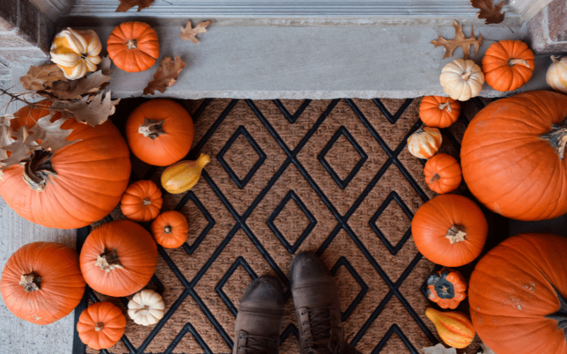 Brown boots walking over brown welcome mat surrounded by fall pumpkins