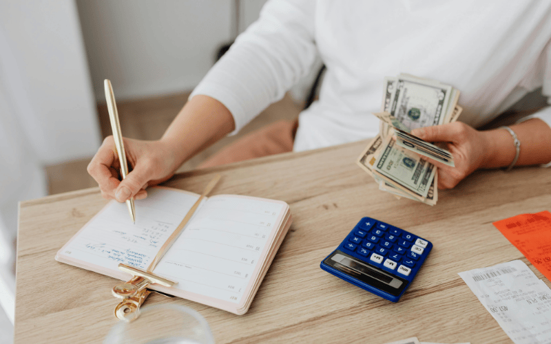 Women's hand writing a budget and holding cash with a calculator planning a home renovation project