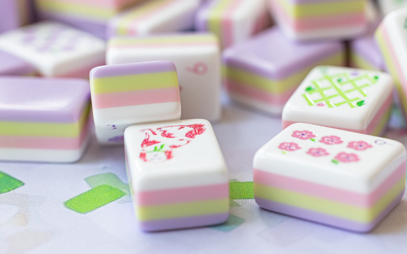 Pretty pastel colored white, pink, green, and purple mah jong tiles spread out on a table 
