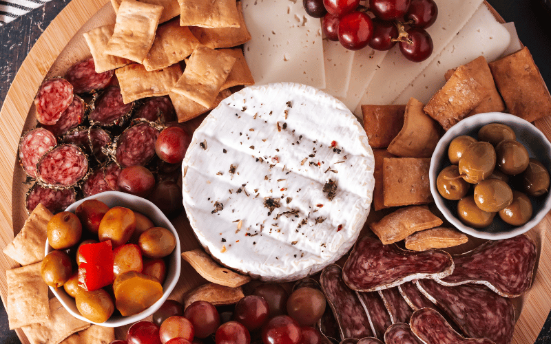 A cheese board with brie cheese, olives, cured meats, and grapes 