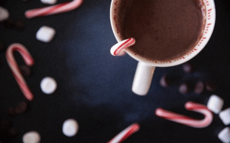 a mug of hot chocolate with marshmallows and candy canes on the table 
