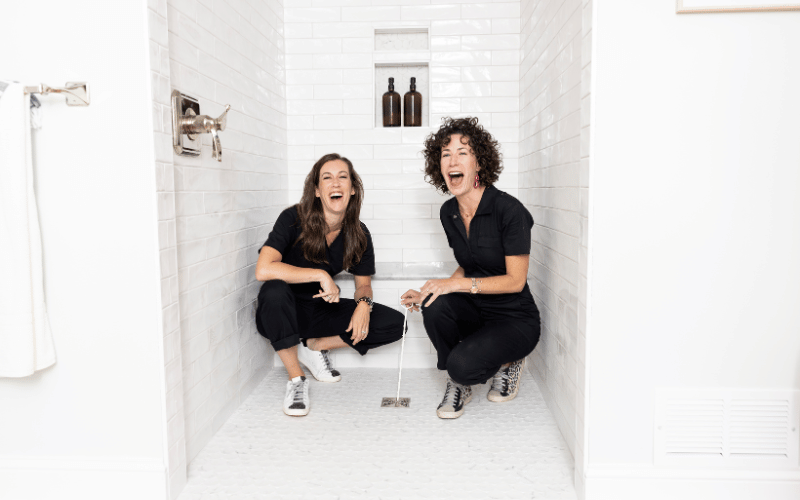 two women wearing black clothes in an all white bathroom 