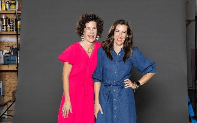 two women standing against a photoshoot backdrop 