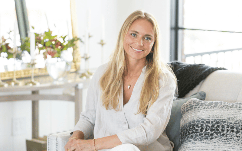 blonde woman sitting on a white couch with plants in the background 