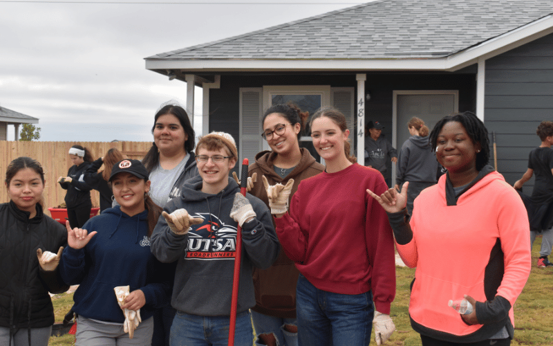 A group of teenagers smiling and standing in front of a large house 