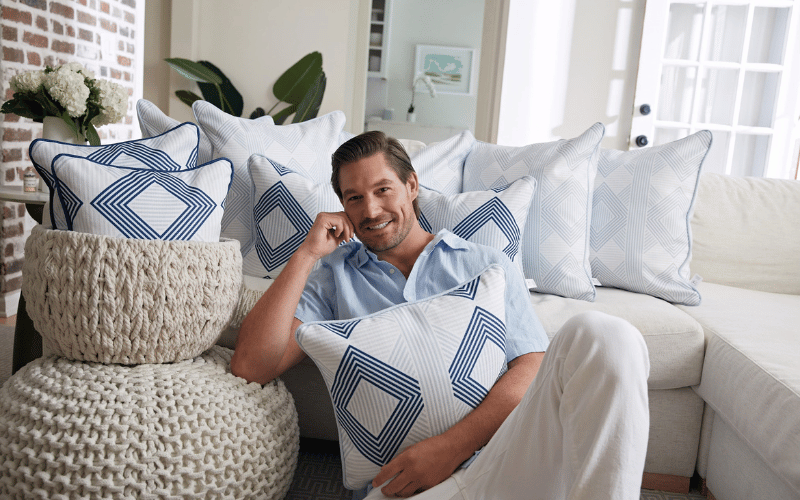 man sitting on a white couch with blue and white pillows 