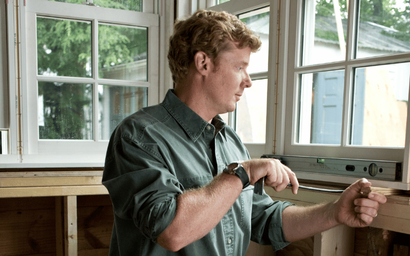 man with ginger hair wearing a green shirt standing near a window 