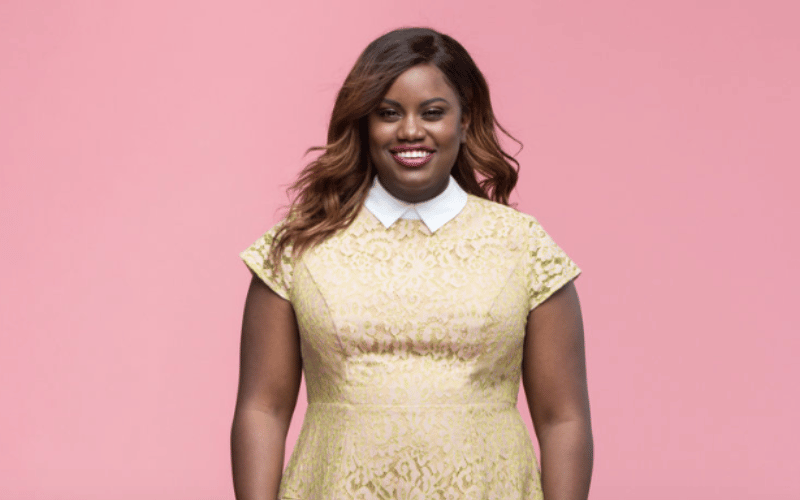 woman wearing a pale yellow dress with a pink background behind her 