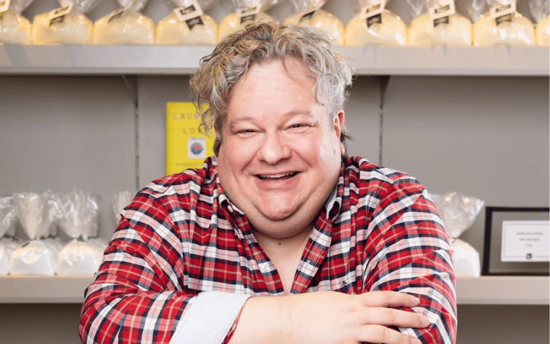 a man wearing a red checked shirt standing in front of a large shelf 