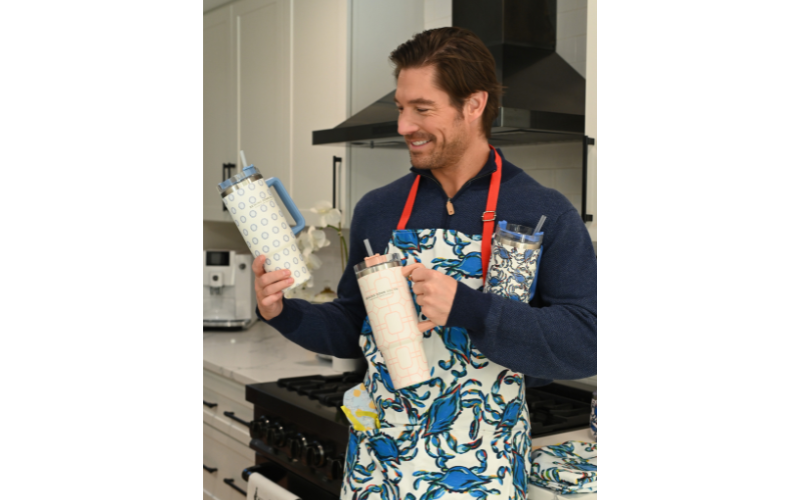 Craig Conover wearing a kitchen apron and holding two water tumblers 