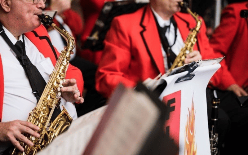 two men carrying trumpets wearing red jackets 