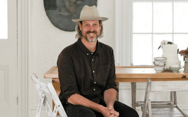 man wearing a black button down shirt and a felt hat sitting at a wooden table