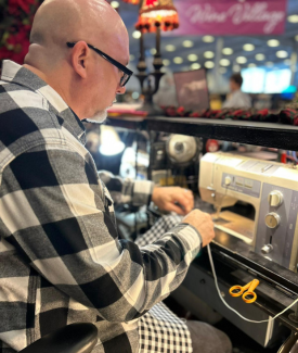 A male vendor wearing a black and white checkered coat sewing on site at the show