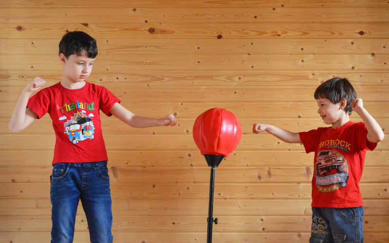 Two young boys wearing red tshirts exercising punching at punching ball having fun