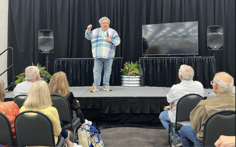 Patric Richardson The Laundry Guy wearing blue and purple pastel dress shirt presenting live on stage at the North Atlanta Home Show to a full audience