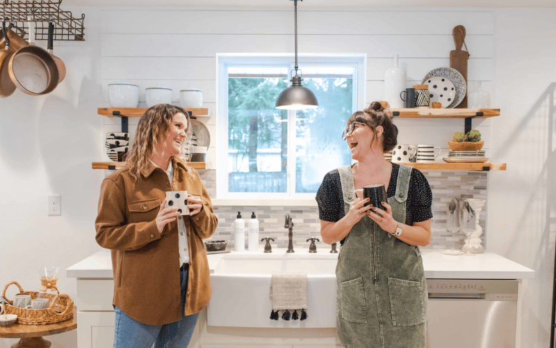 Leslie Davis and Lyndsay Lamb drinking coffee and smiling and laughing together in a renovated laundry room