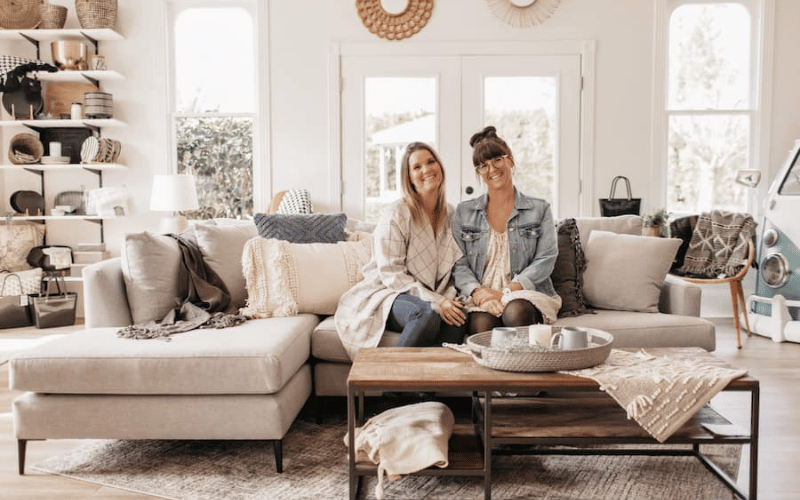 Leslie Davis and Lyndsay Lamb sitting together smiling on a couch in a newly designed modern living room
