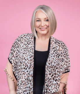 Leigh-Ann Allaire Perrault headshot wearing black shirt and leopard print throw over against baby pink backdrop 