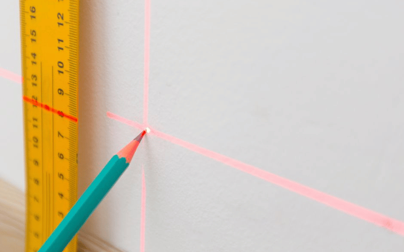 Teal Pencil making dot on white wall using ruler and laser measure