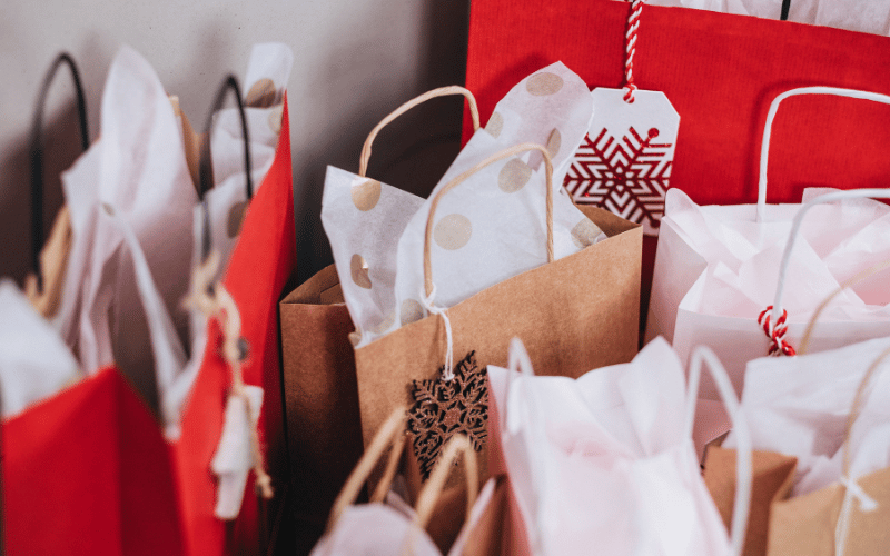 gift giving pile of gift bags in beige, red and white of presents purchased for loved ones