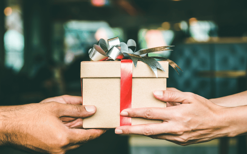 gift giving close up of male hands handing beige wrapped present with red bow to female hands