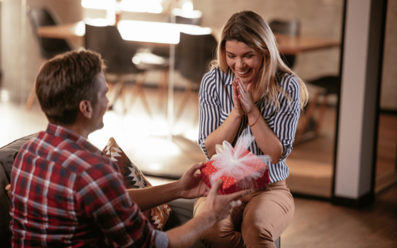 Gift Giving man wearing red plaid shirt gifting his happy girlfriend weaing striped tshirt a beautiful small red gift box with a white bow