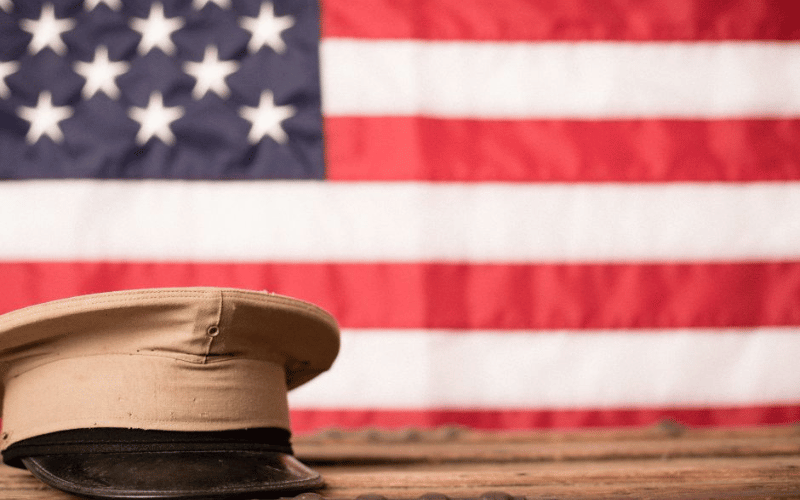 Image of military hat on wooden bench against US Flag backdrop