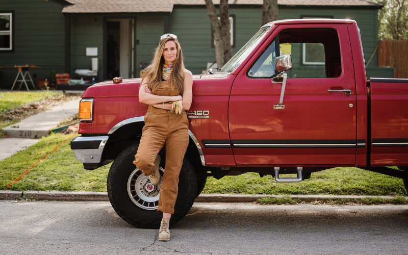 Kim_Wolfe_Wearing_Brown_Overalls_Leaning_IntoRed_Pickup_Truck